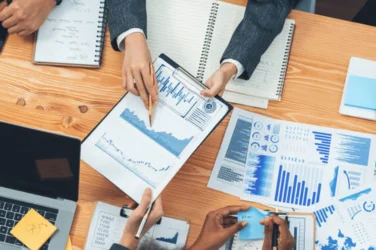 A business team is using a laptop to analyze data while laying out charts and documents